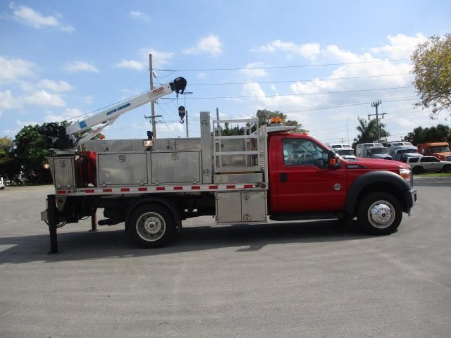 A red truck with a crane attached to it is parked in a parking lot.