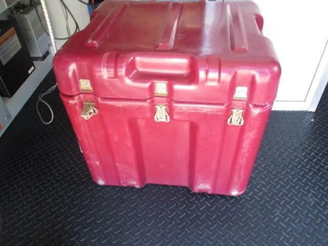 A red plastic trunk with a handle is sitting on a black floor