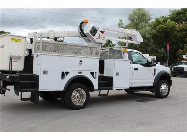 A white utility truck with a bucket on the back is parked in a parking lot.