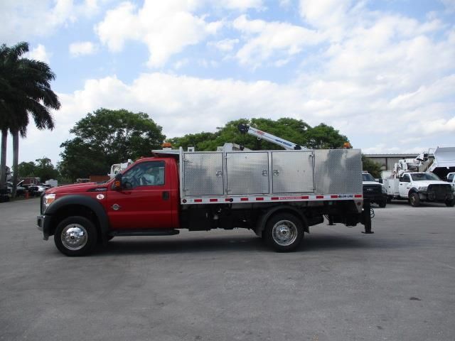 A red truck is parked in a parking lot with palm trees in the background