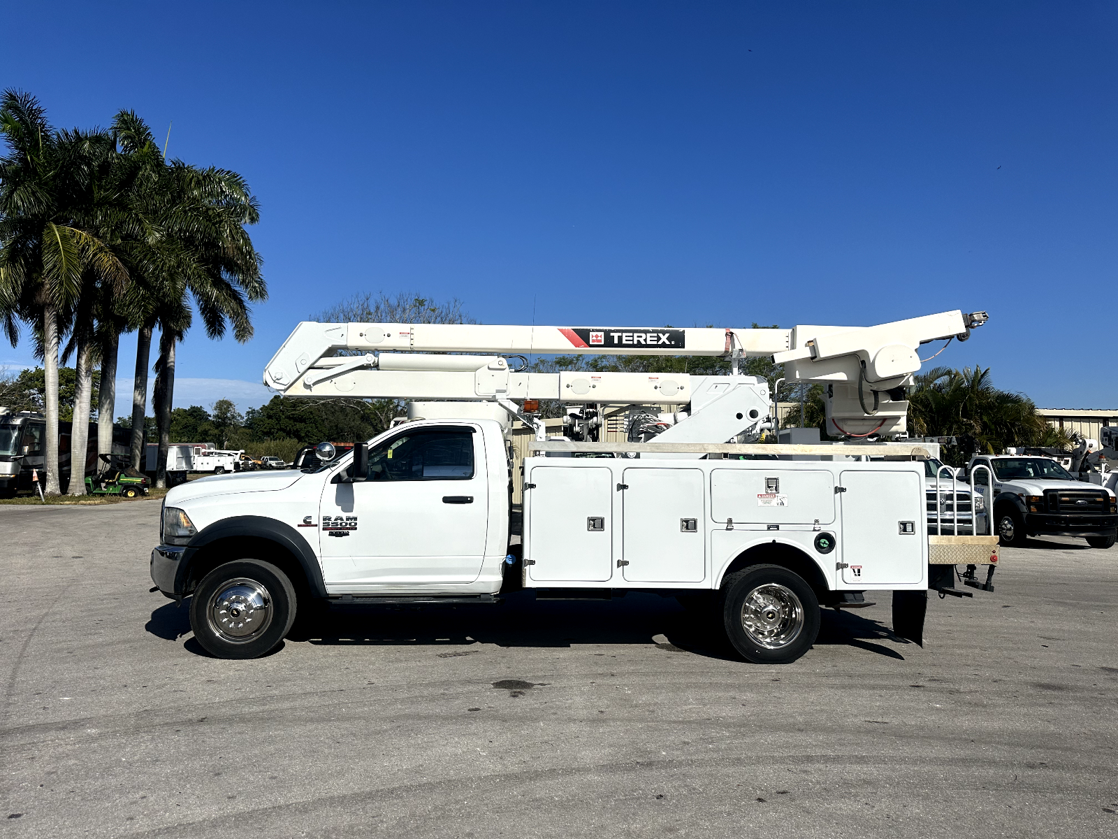 A white utility truck with a crane on the back is parked in a parking lot.