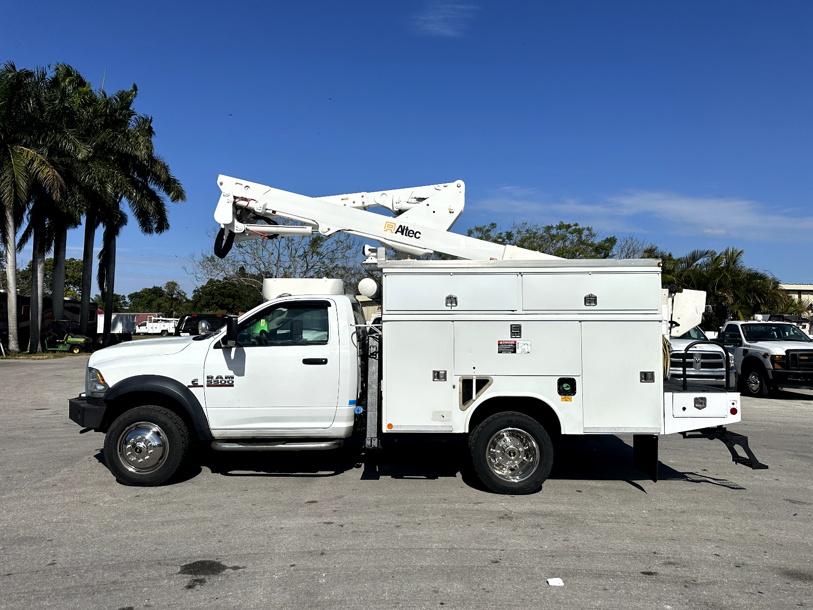 A white utility truck with a crane on top of it is parked in a parking lot.