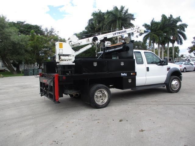 A white truck with a crane on the back is parked in a parking lot.