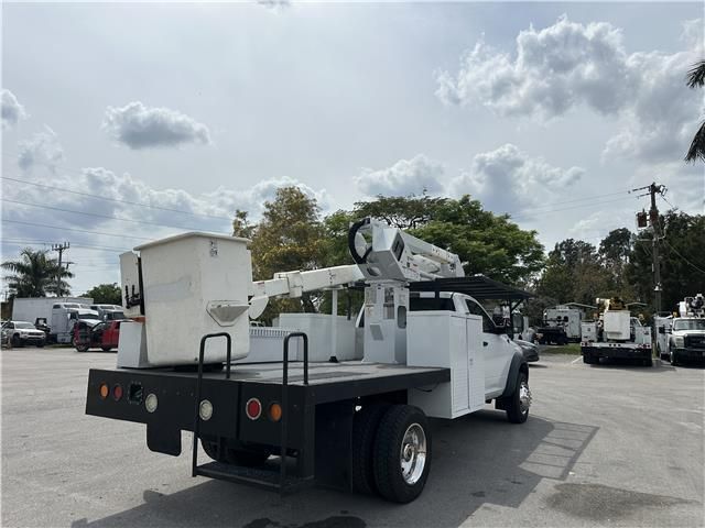 A white truck with a bucket on the back is parked in a parking lot