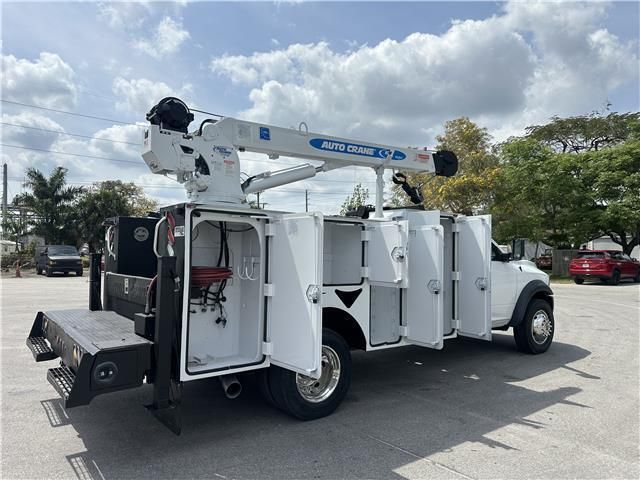 A white service truck with a crane on the back is parked in a parking lot.