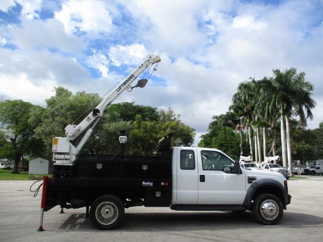 A white truck with a crane attached to it is parked in a parking lot.