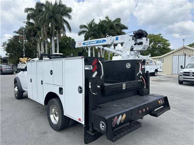 A white service truck with a crane on the back is parked in a parking lot.