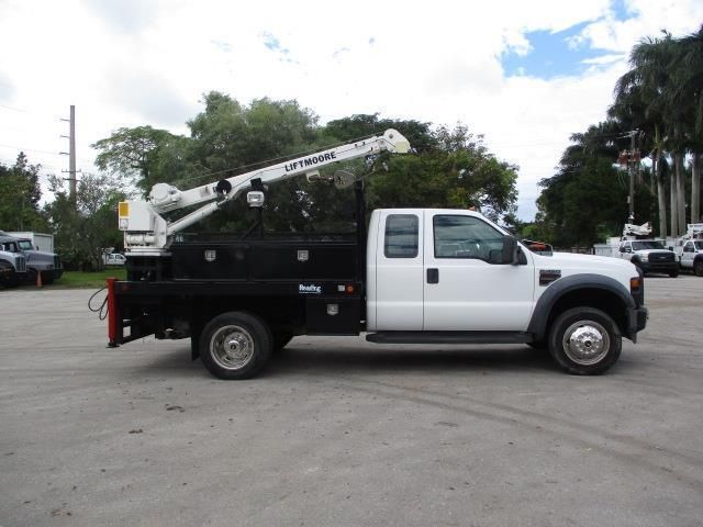 A white truck with a crane on the back is parked in a parking lot.