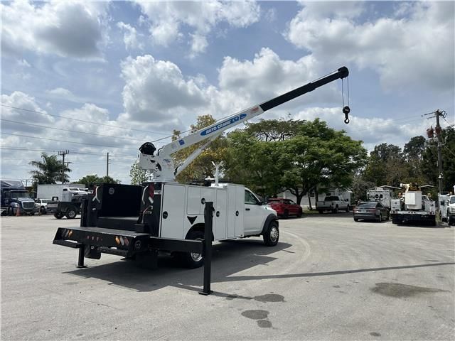 A white truck with a crane attached to the back is parked in a parking lot.
