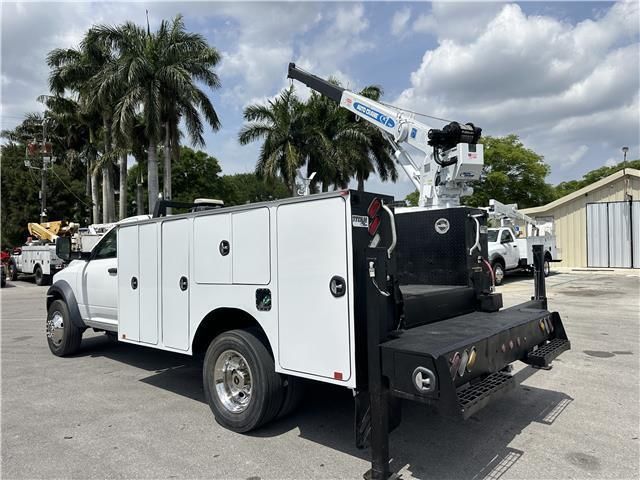 A white service truck with a crane on the back is parked in a parking lot.