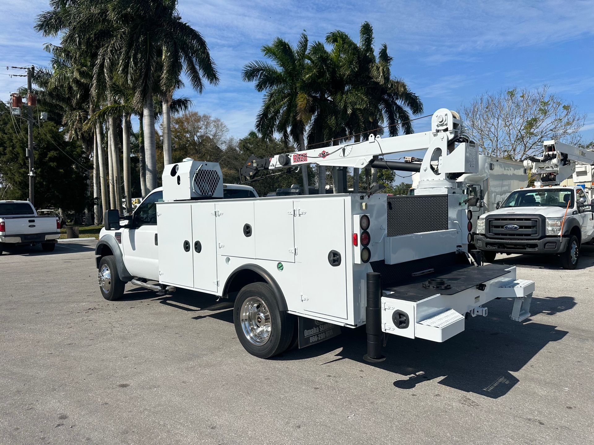 A white utility truck with a crane on the back is parked in a parking lot.