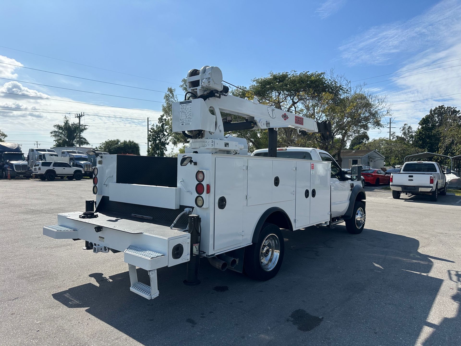 A white utility truck with a crane on the back is parked in a parking lot.