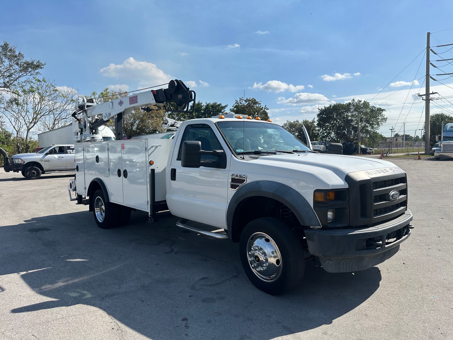 A white truck with a crane on top of it is parked in a parking lot.