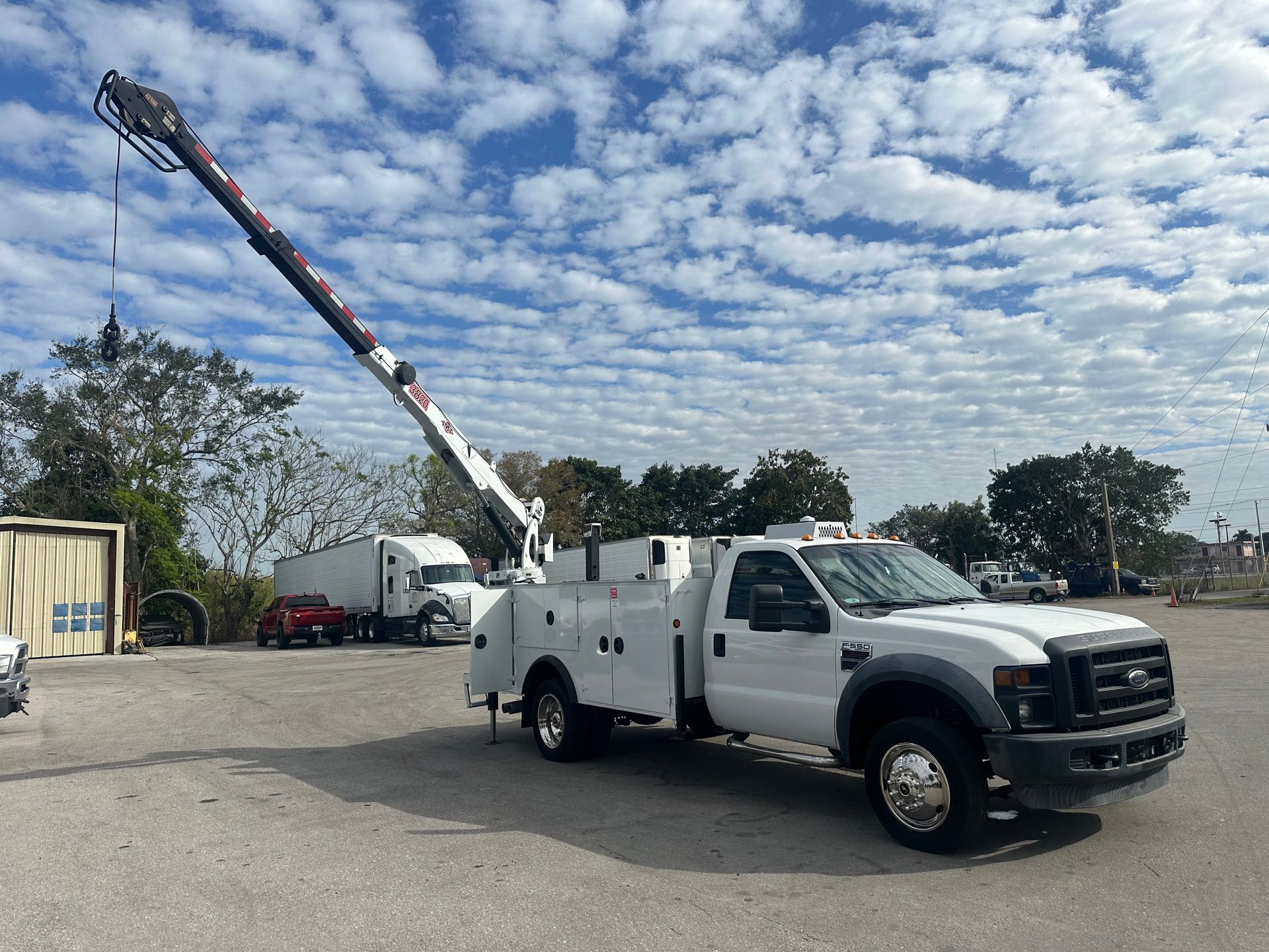 A white truck with a crane on top of it is parked in a parking lot.