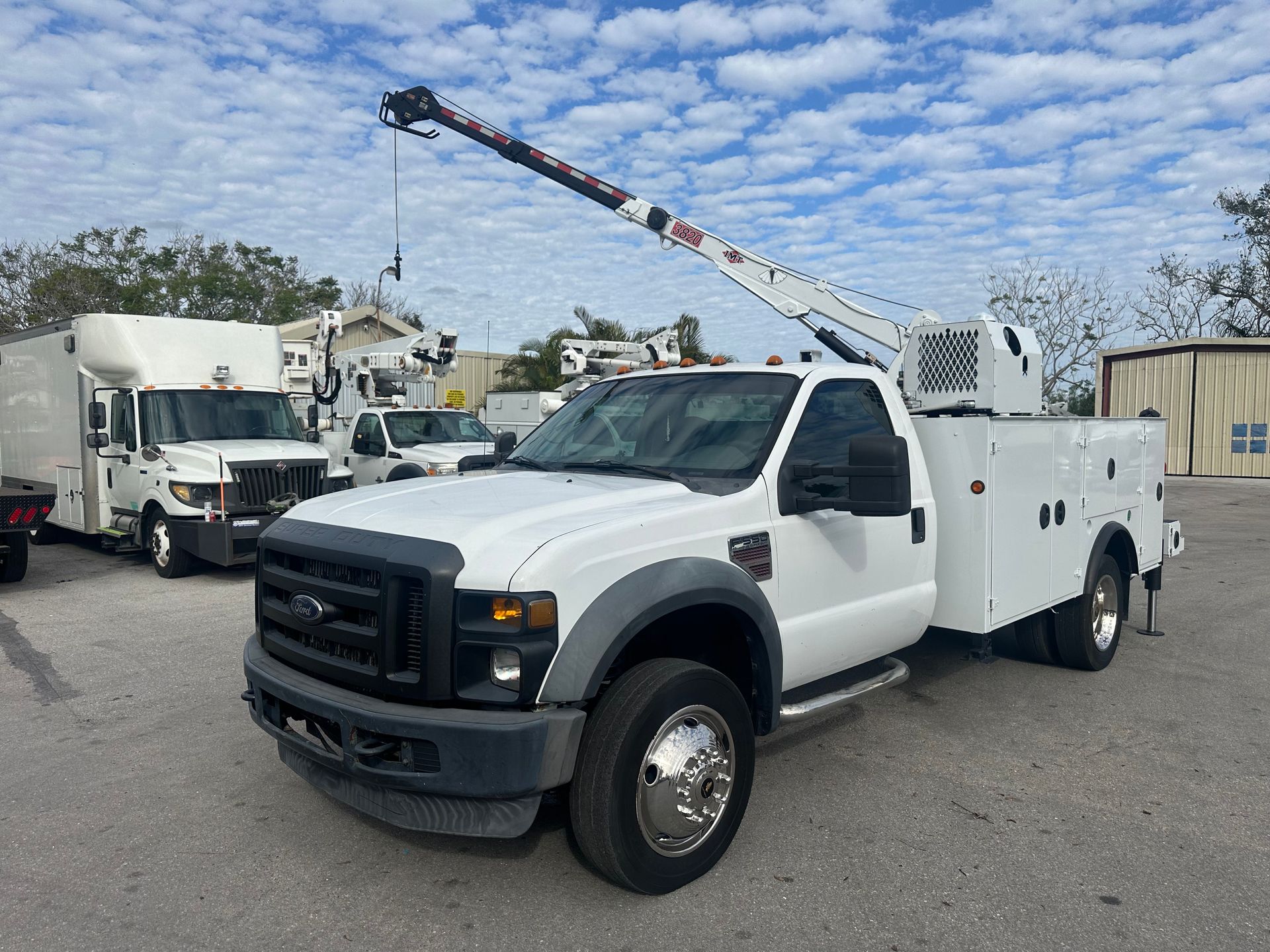 A white truck with a crane on top of it is parked in a parking lot.