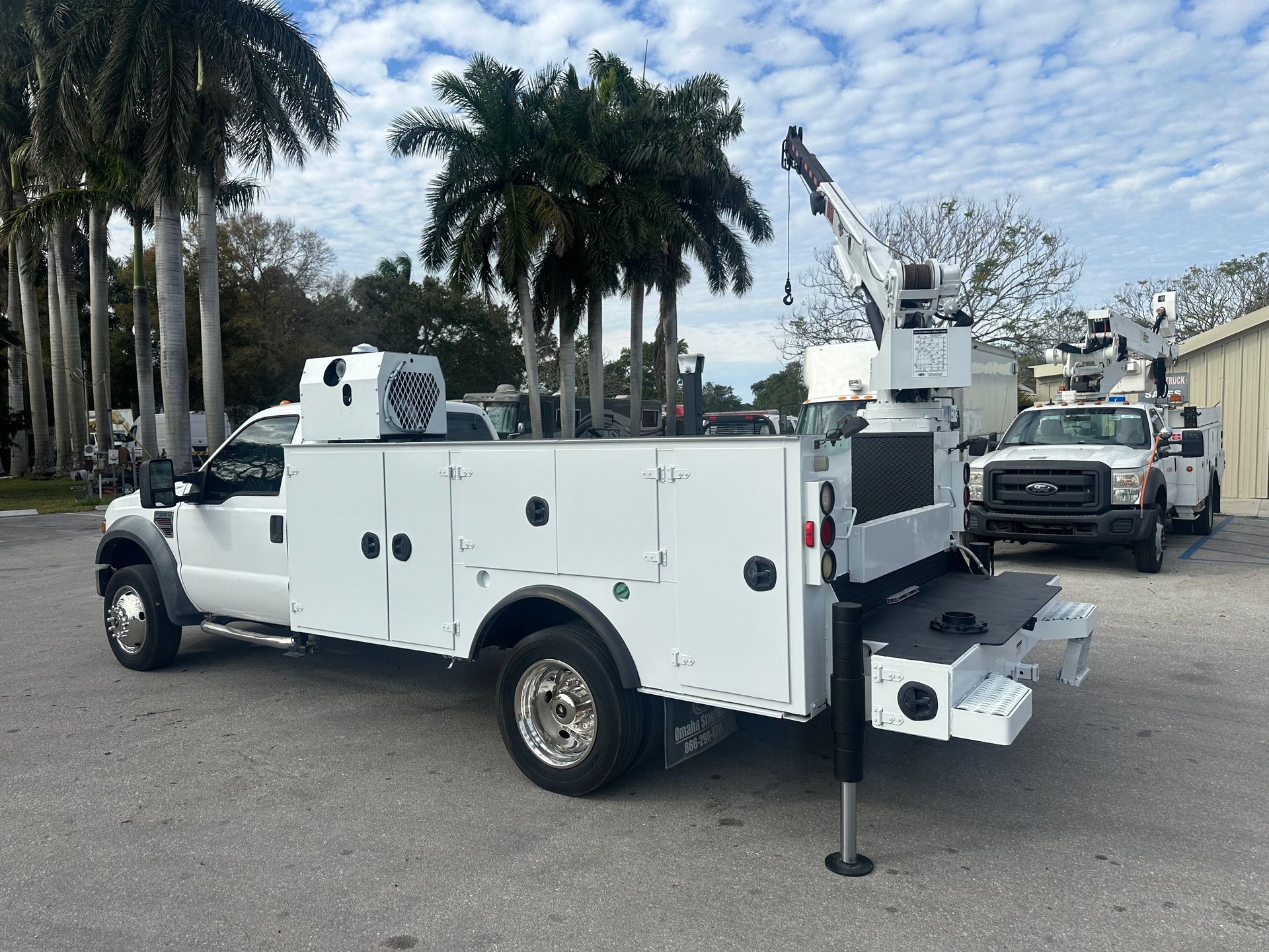 A white utility truck with a crane on the back is parked in a parking lot.