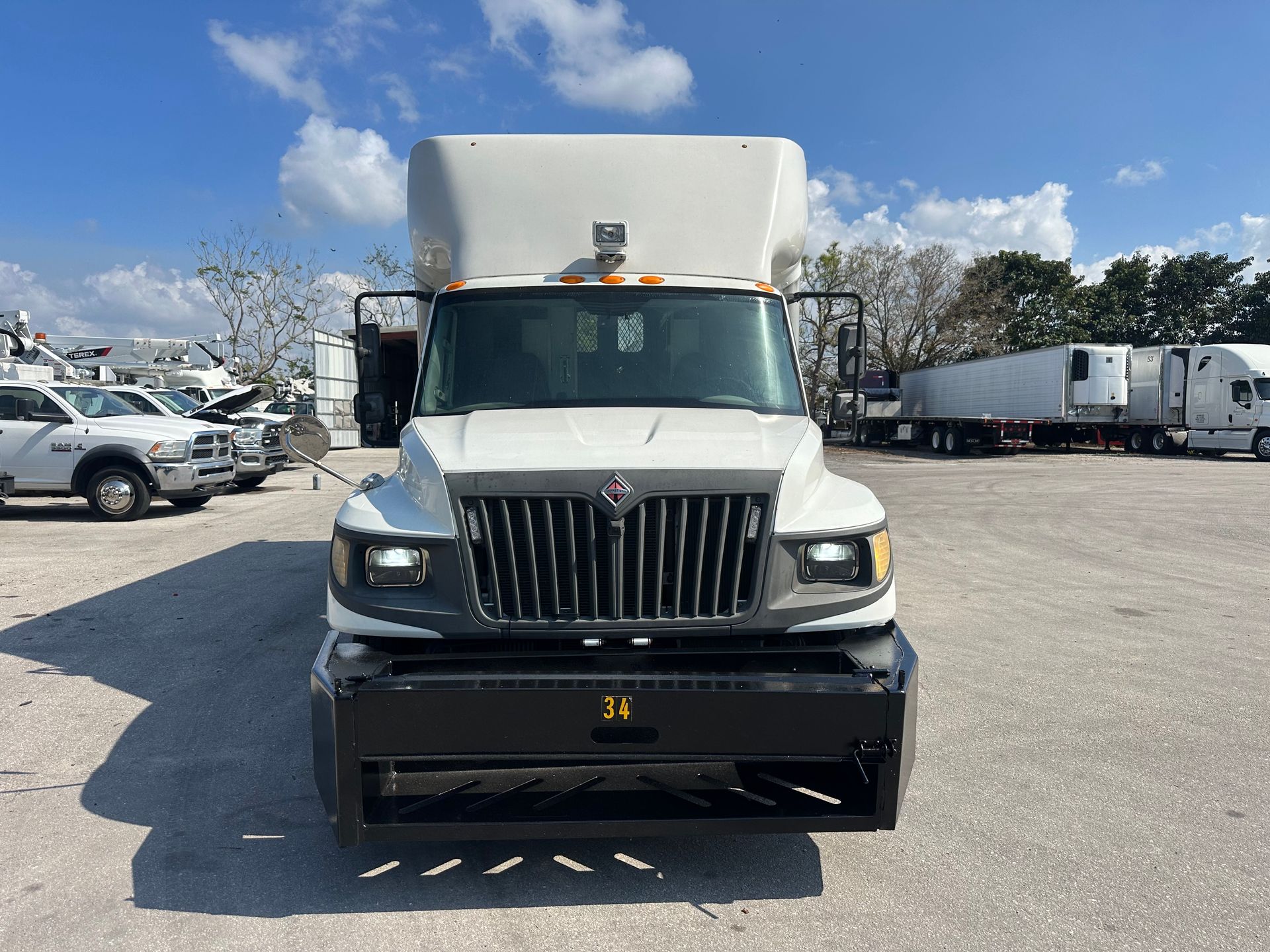 A white truck is parked in a parking lot with other trucks.