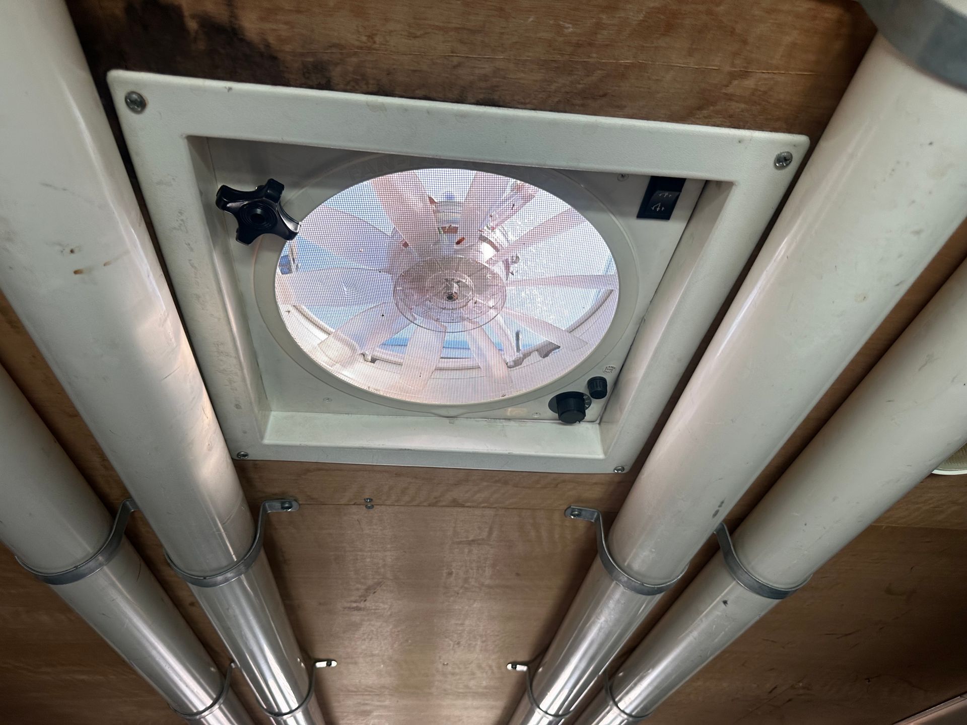 A fan is hanging from the ceiling of a room surrounded by pipes.