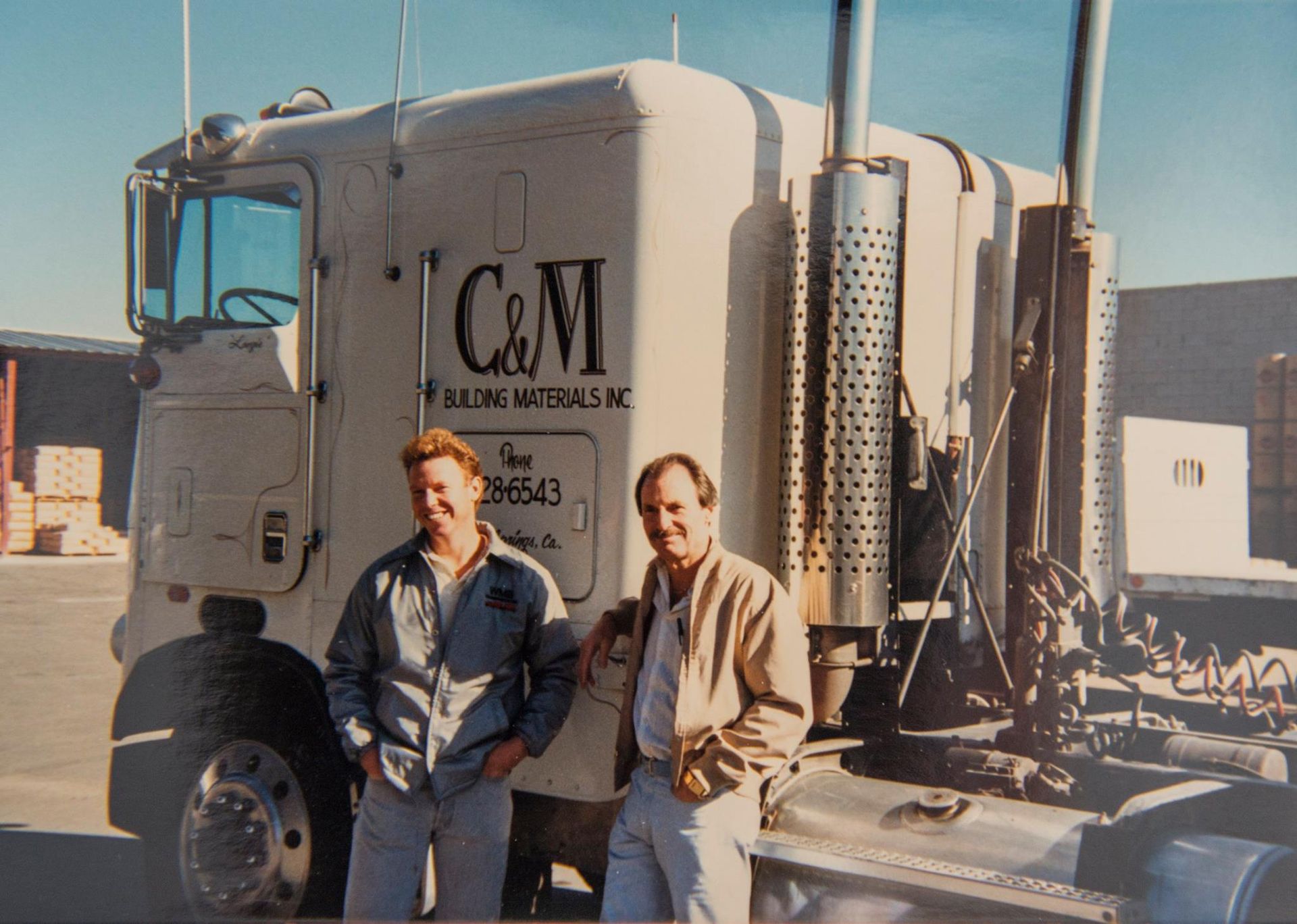 Two men standing in front of a truck that says c & m