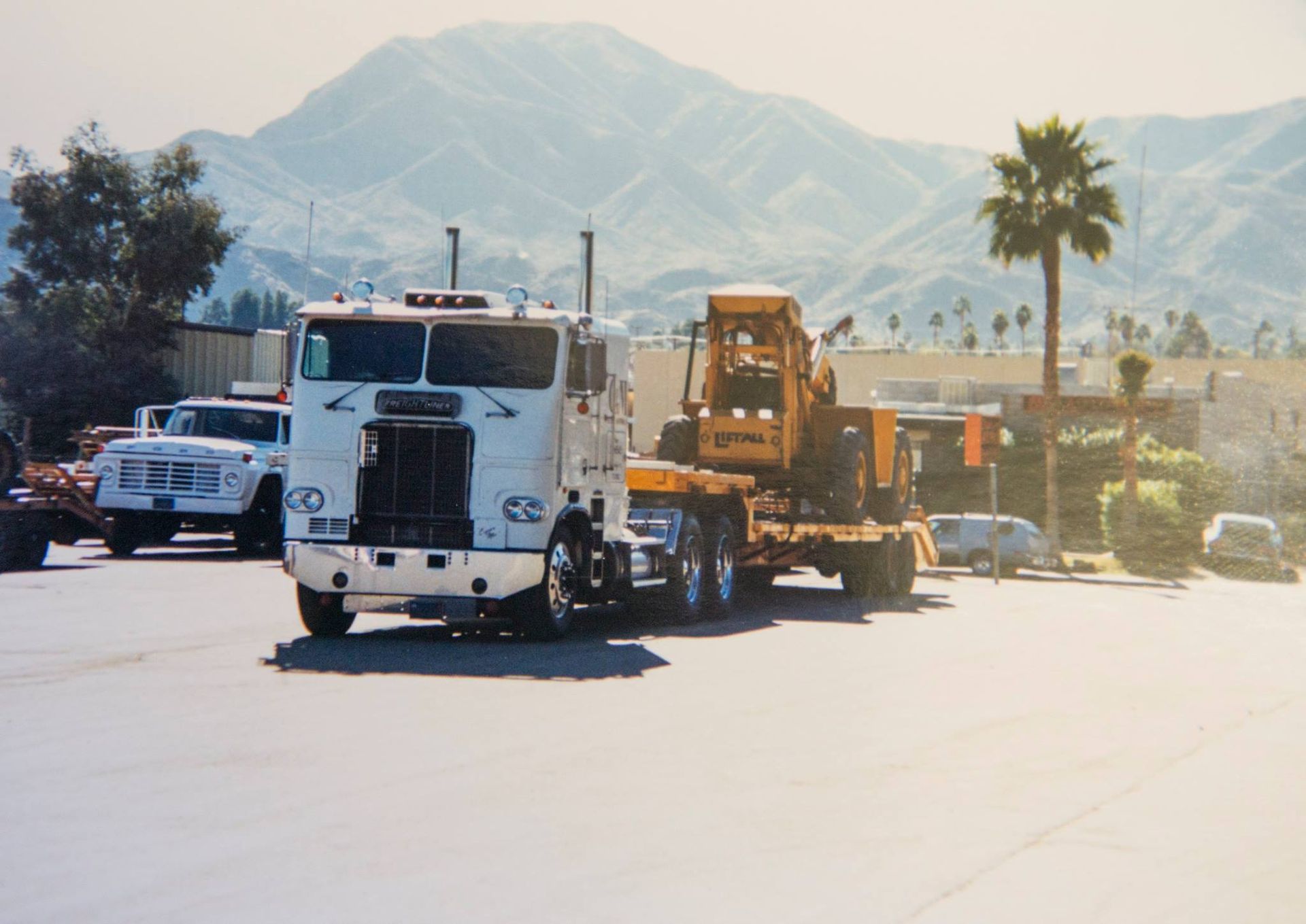 A white semi truck is driving down a road with mountains in the background
