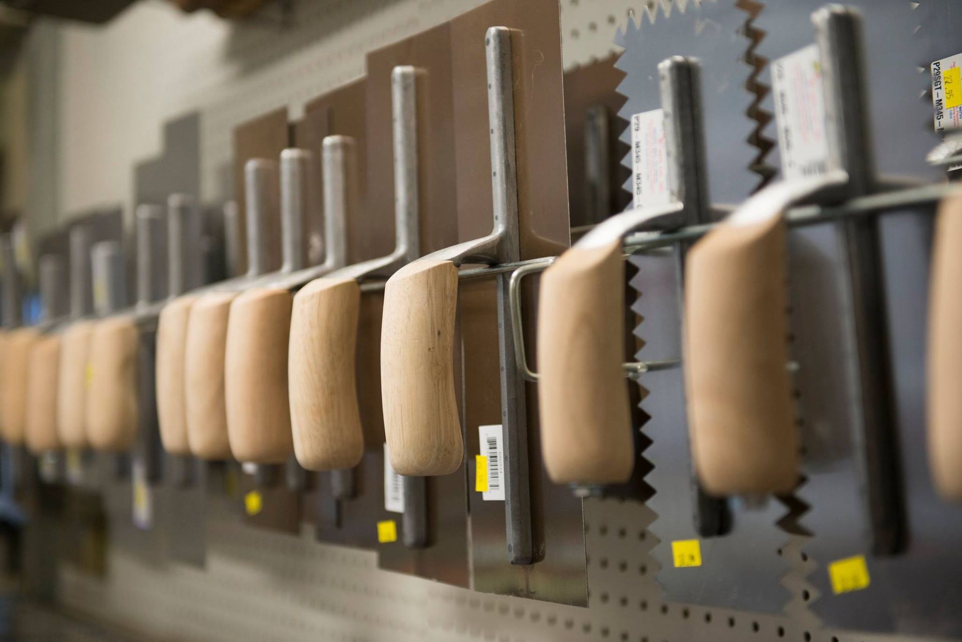 A row of tools with wooden handles are hanging on a wall.