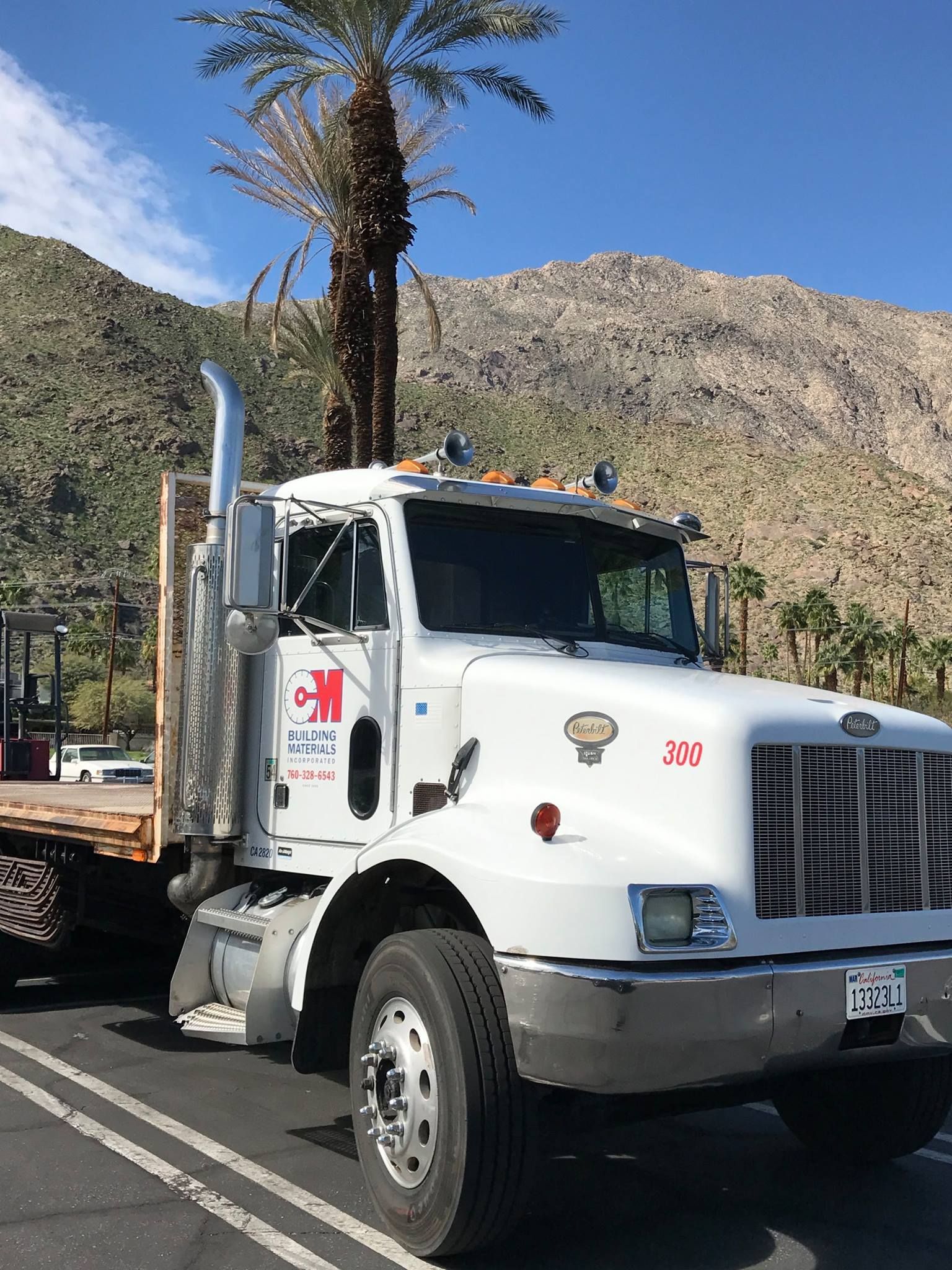A white semi truck is parked in a parking lot with mountains in the background.