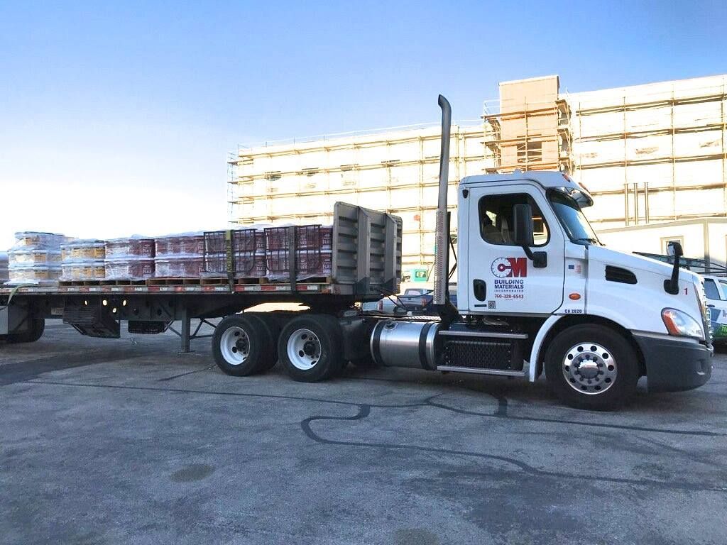A semi truck with a flatbed trailer is parked in front of a building.