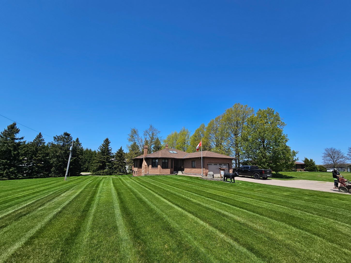 A brick house with a Canadian flag on a bright blue sky day. Striped green lawn in front.
