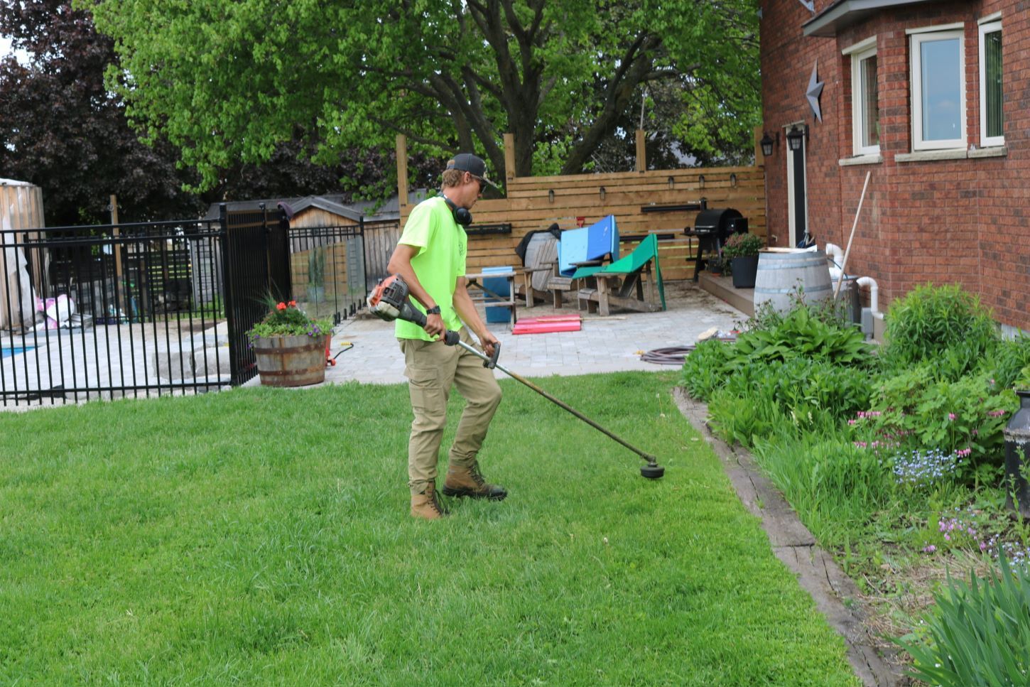 A person using a weed wacker on a green lawn next to a flower bed, backyard setting.