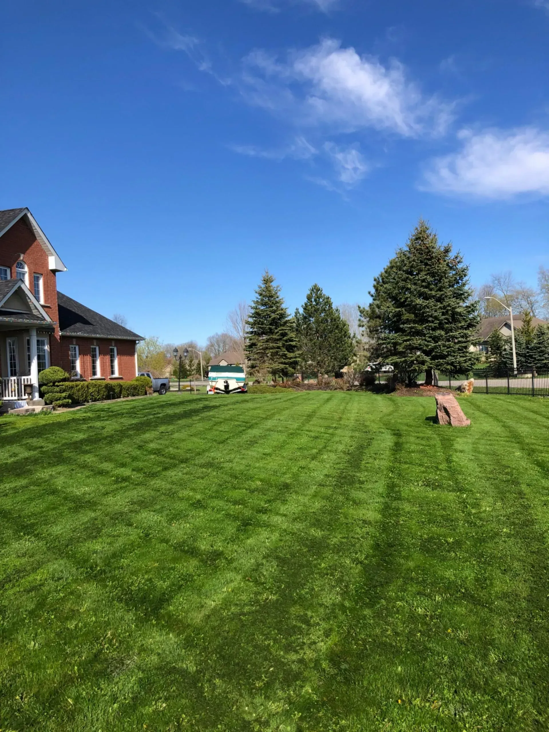 Green lawn with fresh mowing lines, brick house on the left, trees in the middle, and blue sky.
