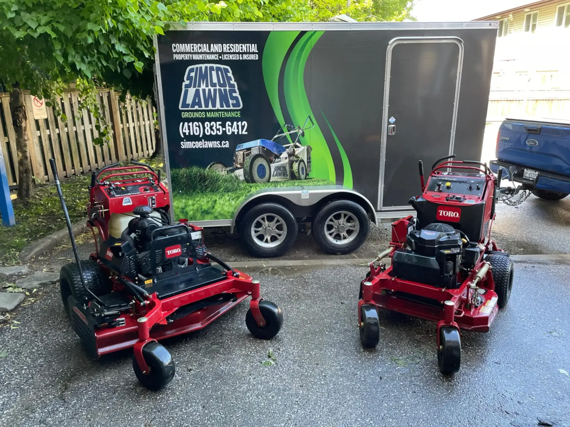 Two red lawn mowers in front of a trailer with