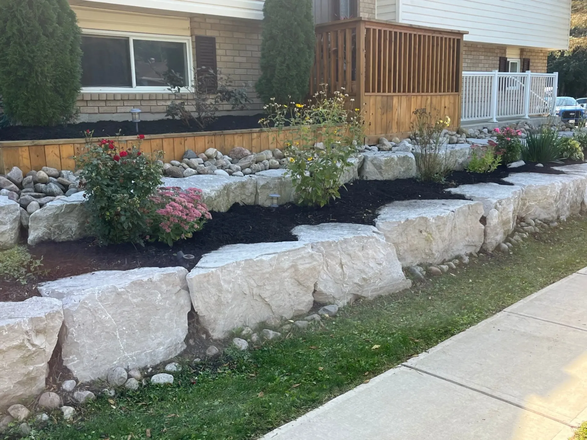 Stone retaining wall with flowers and plants in front of a house.