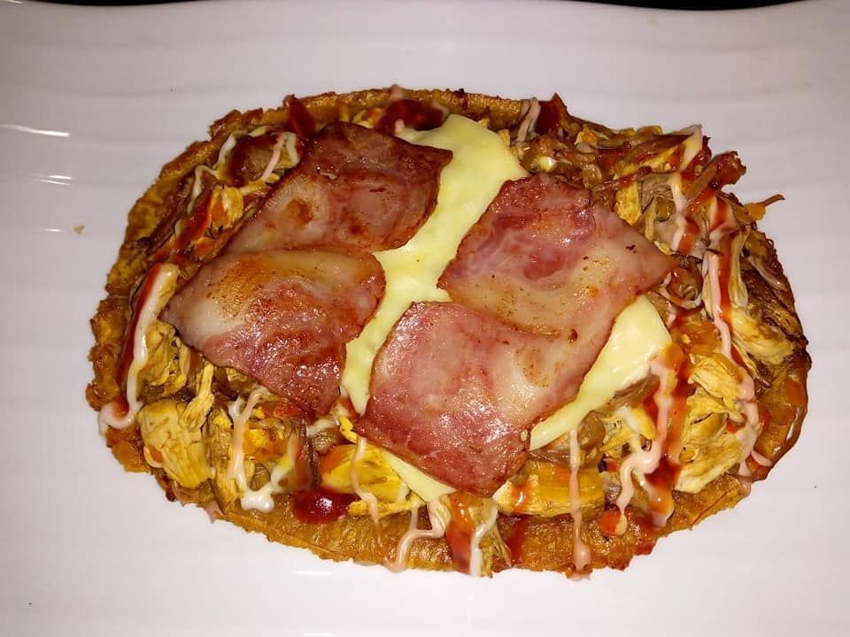 Pizza de pollo y tocino con queso derretido, salsas rociadas, en un plato blanco.