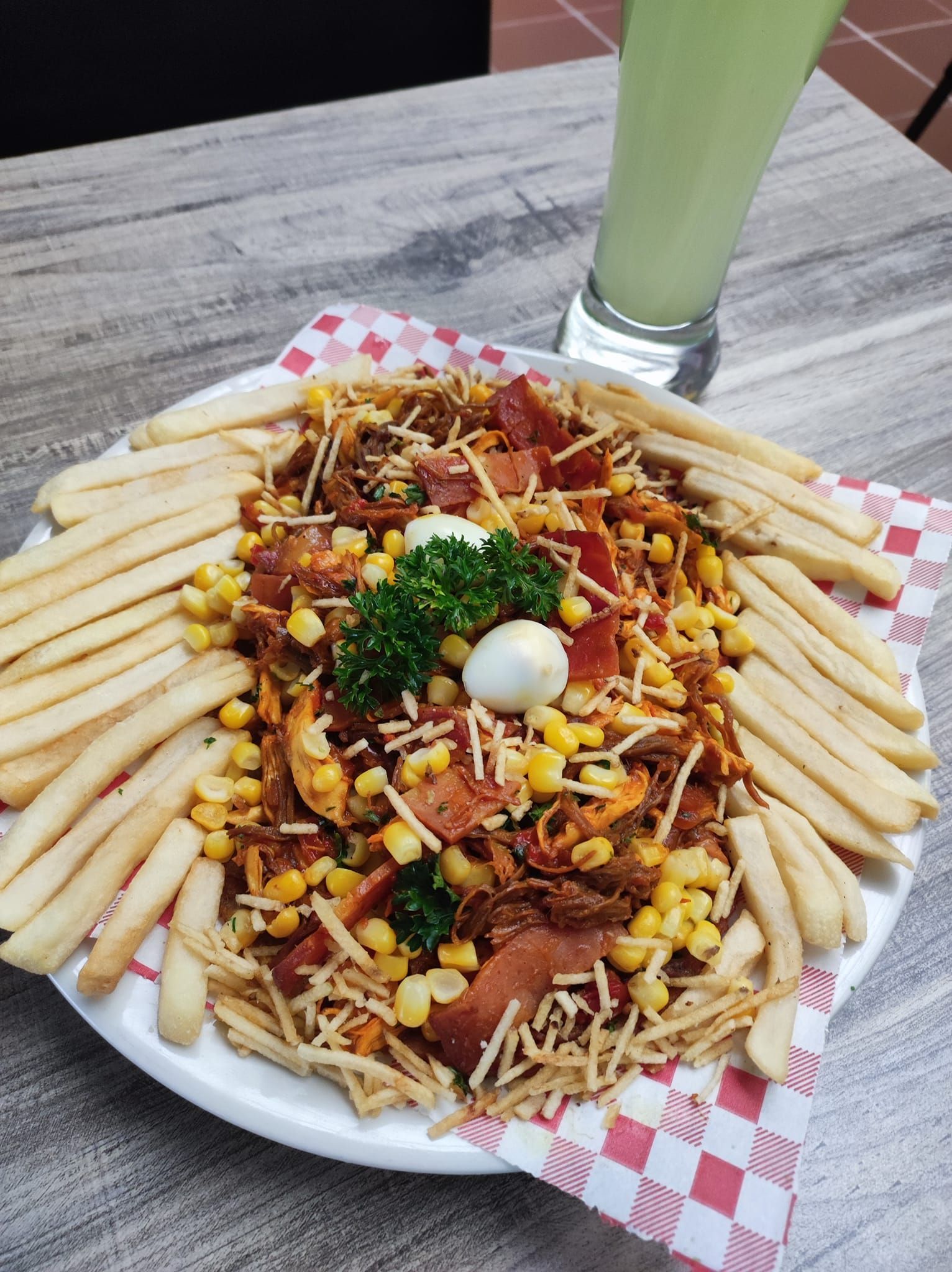 Plato de papas fritas cargadas con maíz, tocino y una bebida.