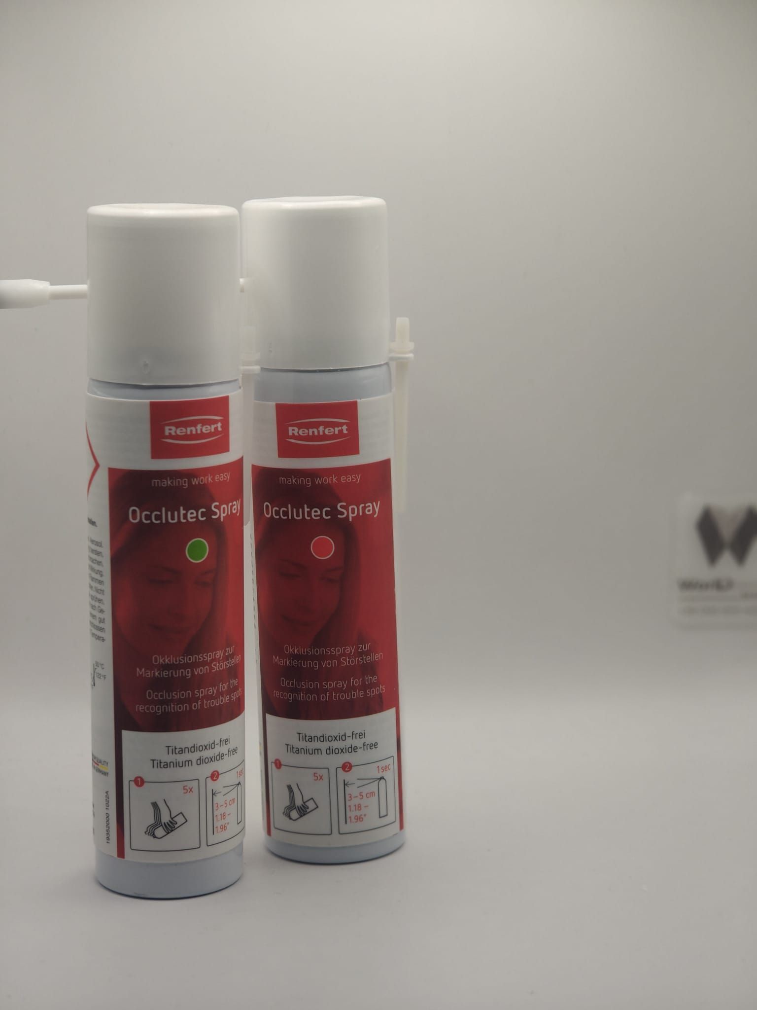 Due bombolette spray bianche identiche con etichette e ugelli applicatori rossi, esposte su uno sfondo bianco uniforme.