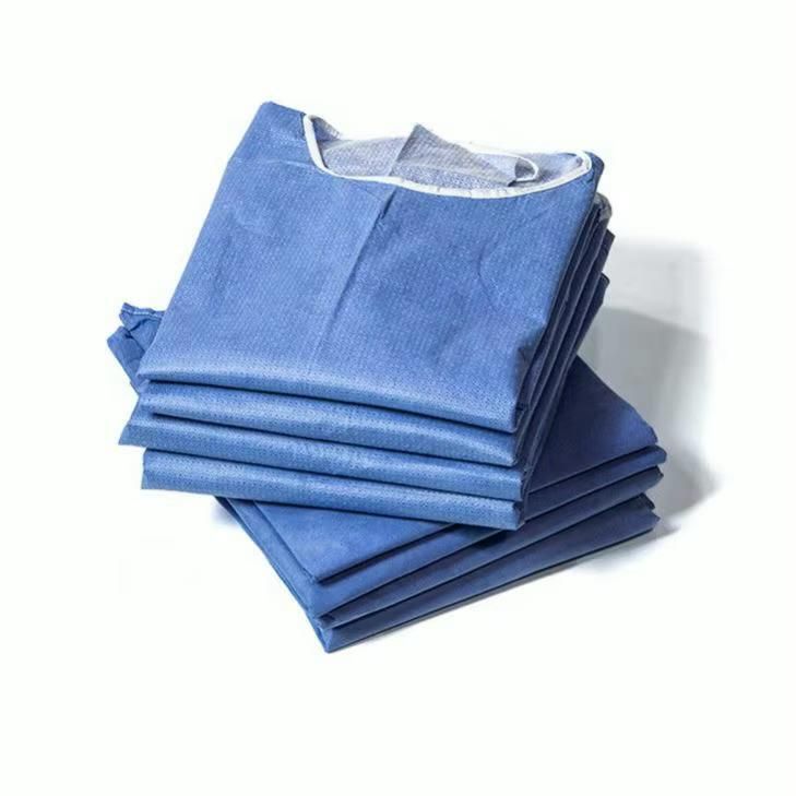 Una pila di camici chirurgici monouso blu piegati su sfondo bianco.