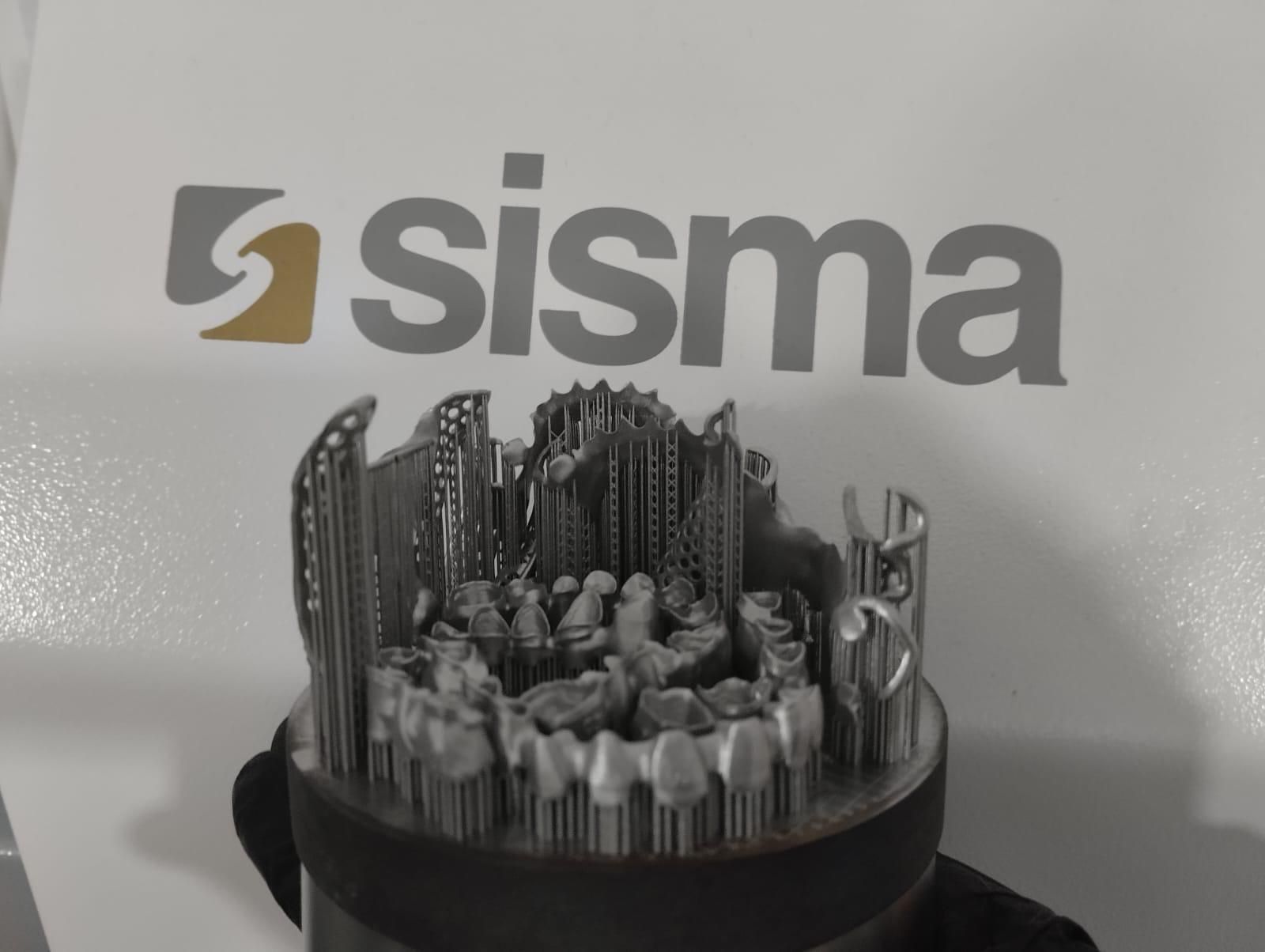 Una struttura dentale in metallo stampata in 3D, composta da diverse corone dentali fissate a una base, con lo sfondo del logo Sisma.
