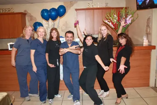 Group of dental office staff celebrating, posing joyfully, with balloons and flowers.