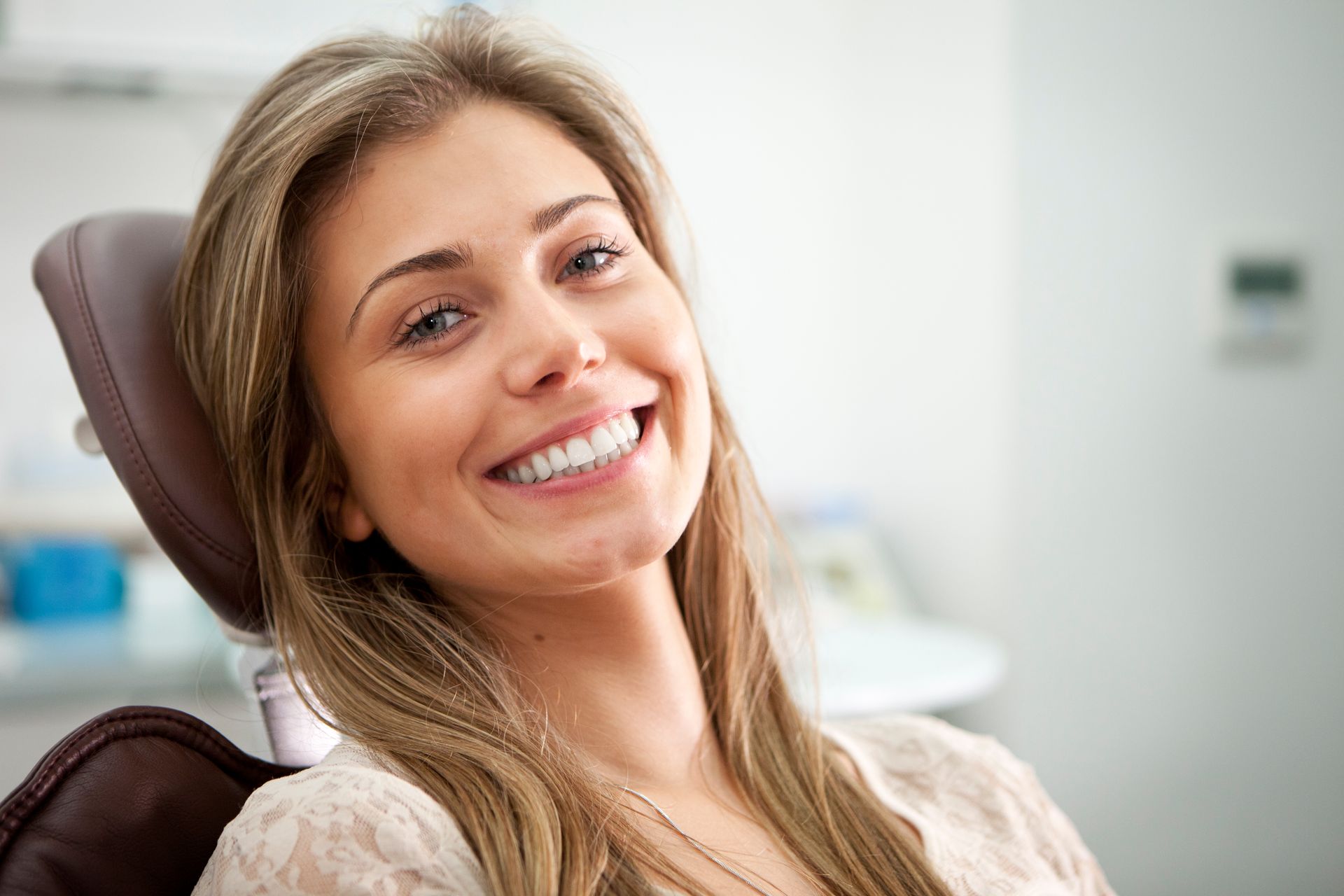 Woman smiling widely in a dental chair, showing white teeth; dental office background.