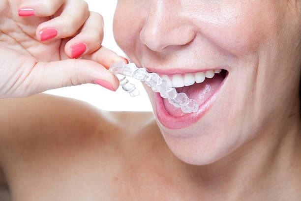 Woman holding clear aligner near her mouth, smiling.