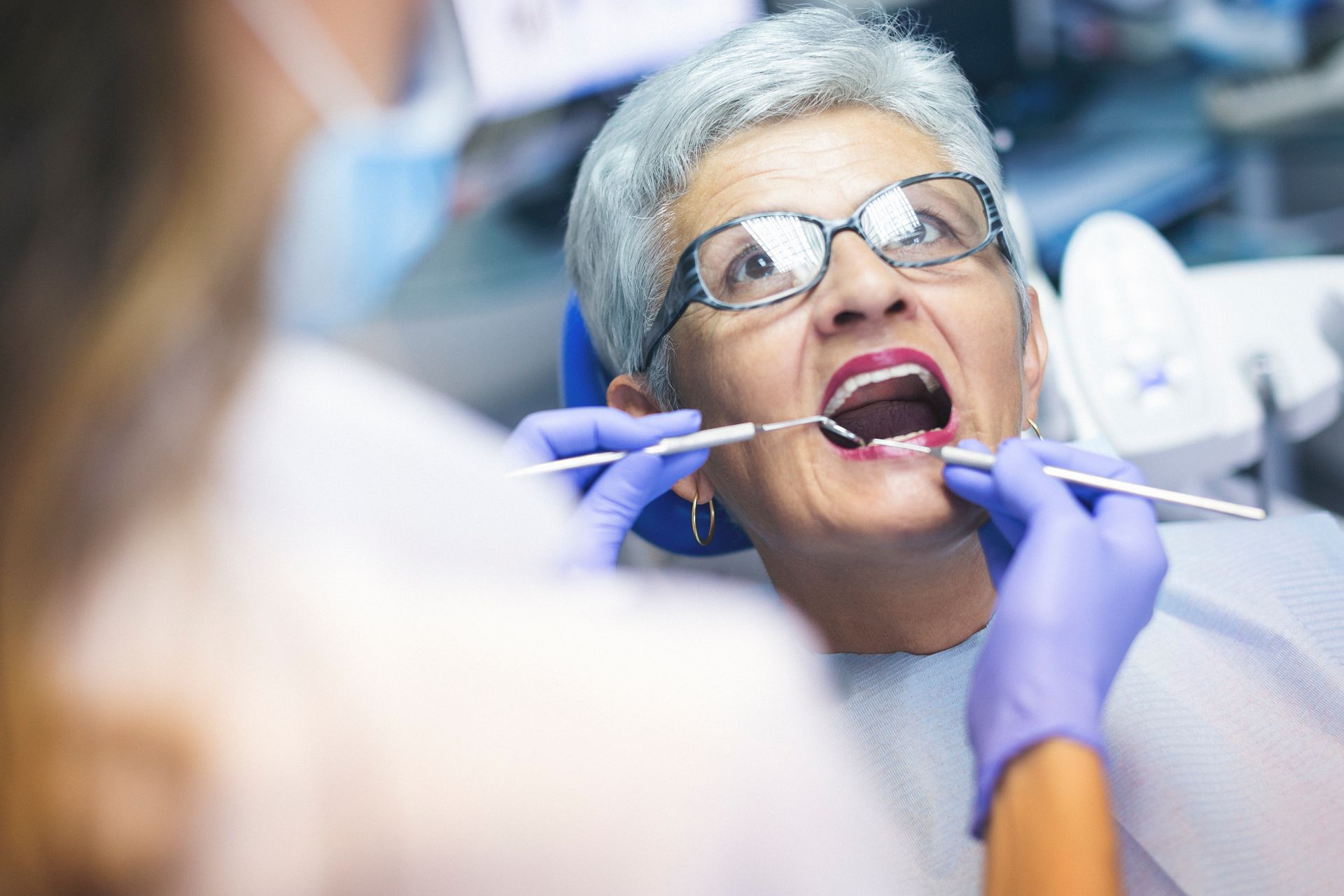 Dentist examining a patient's open mouth with tools in a dental office.