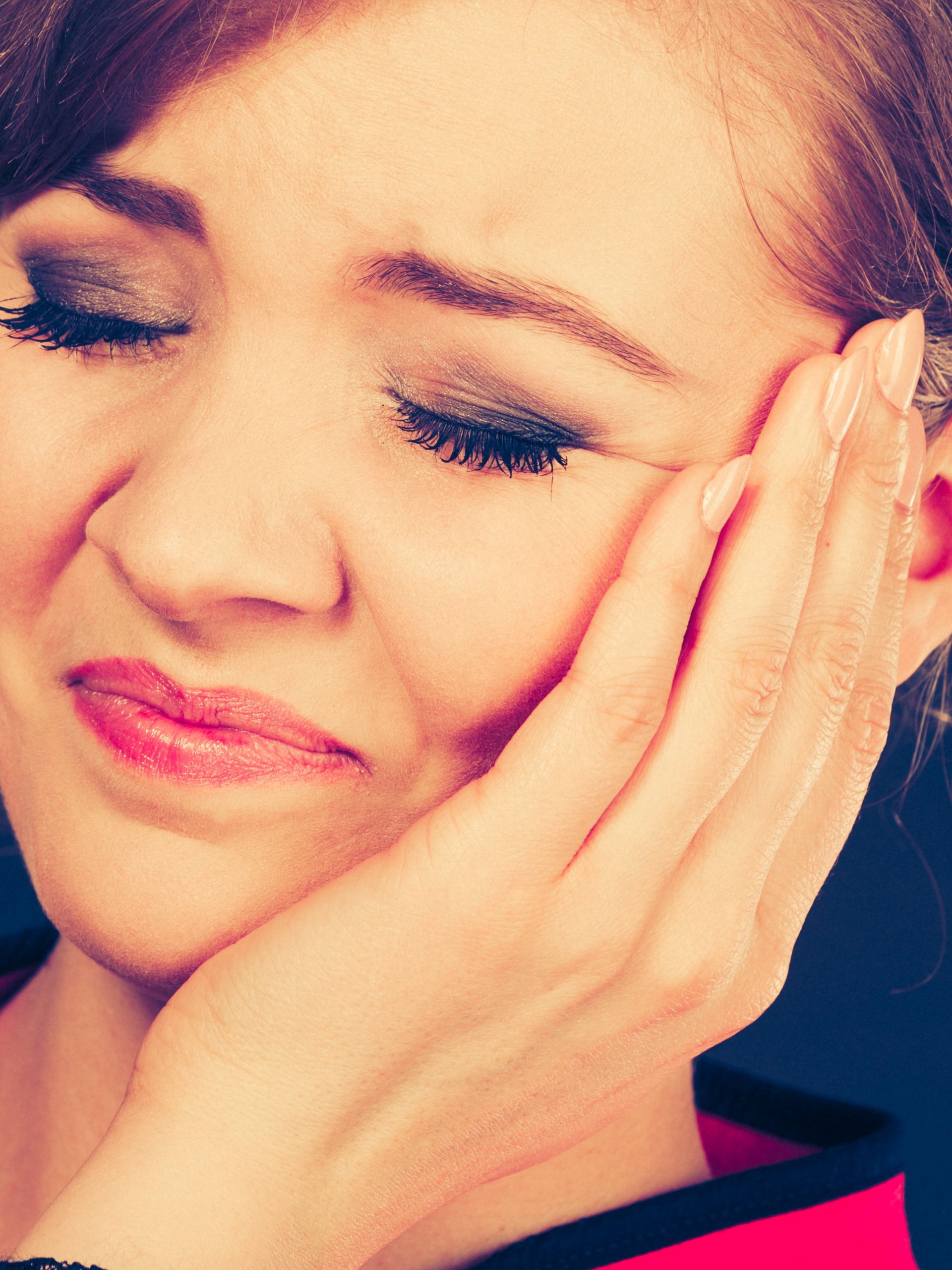 Woman holding cheek, appearing in pain, eyes closed.