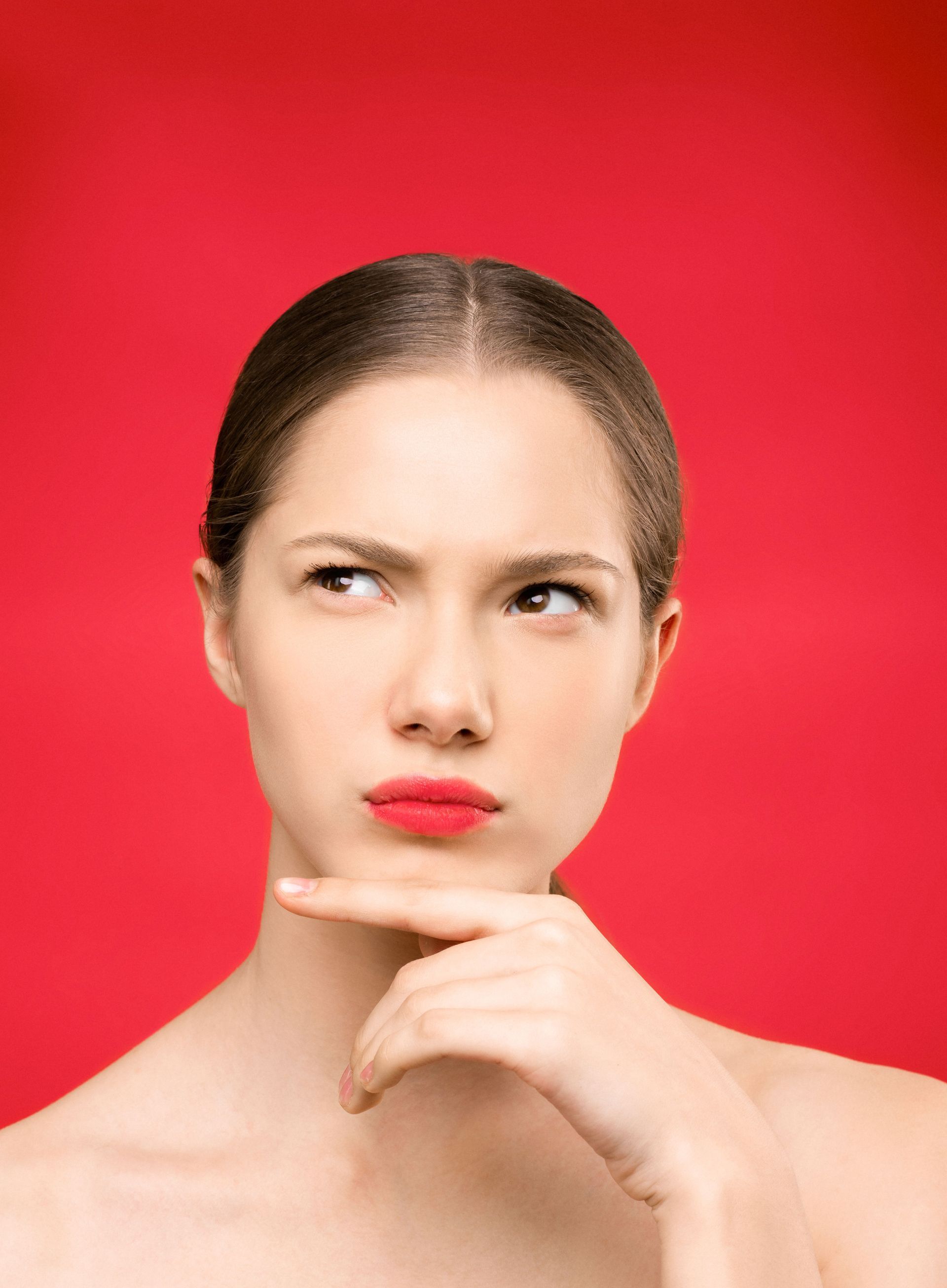 Woman with red lipstick and thoughtful expression against a bright red background