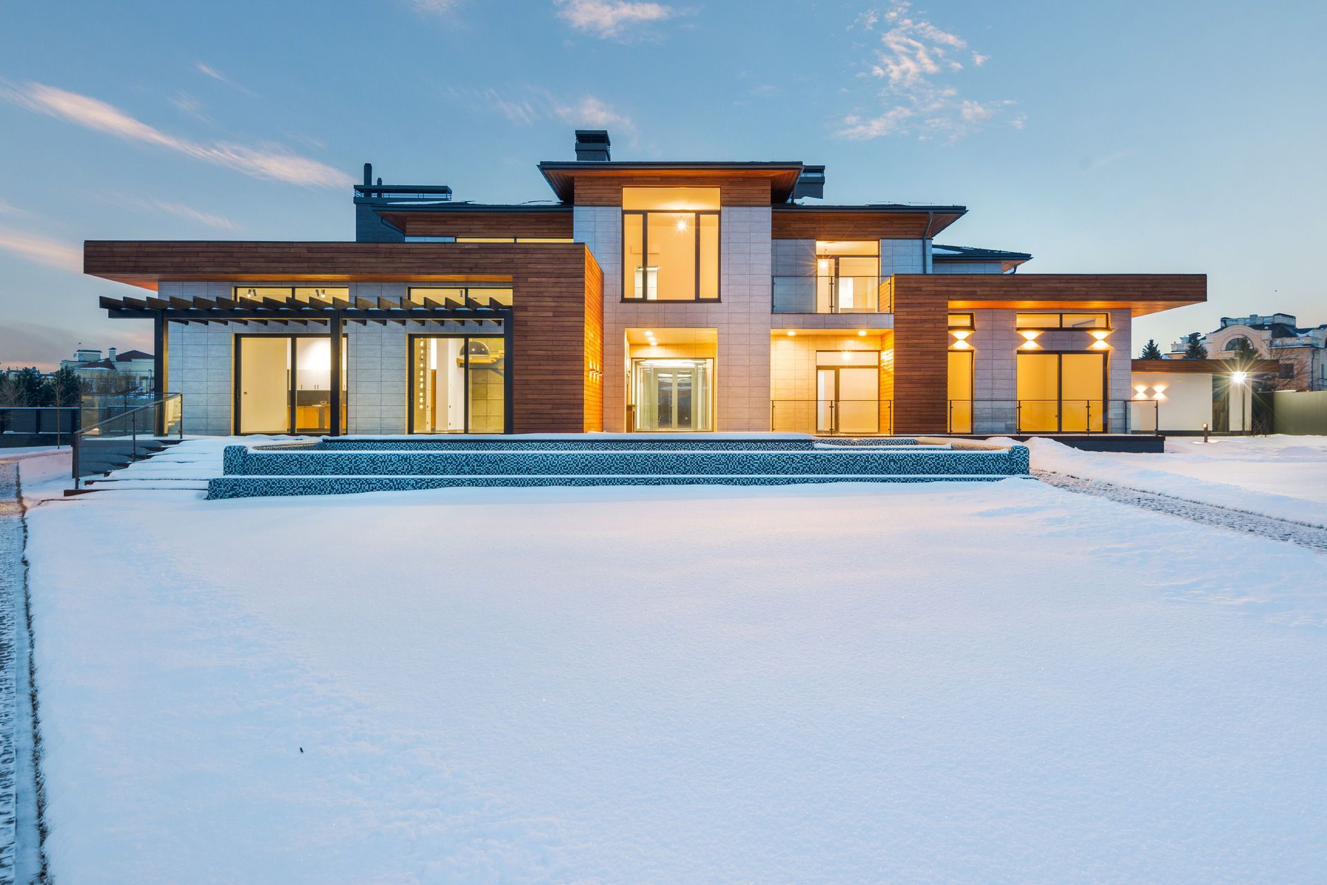 Modern two-story house with warm lights glowing at dusk, surrounded by snow-covered ground