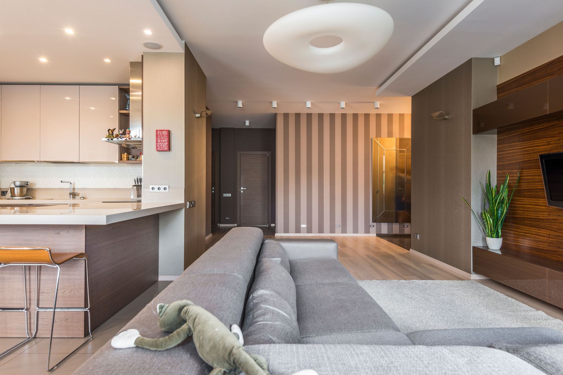 Modern open-plan living room with gray sofa, striped accent wall, and kitchen bar seating