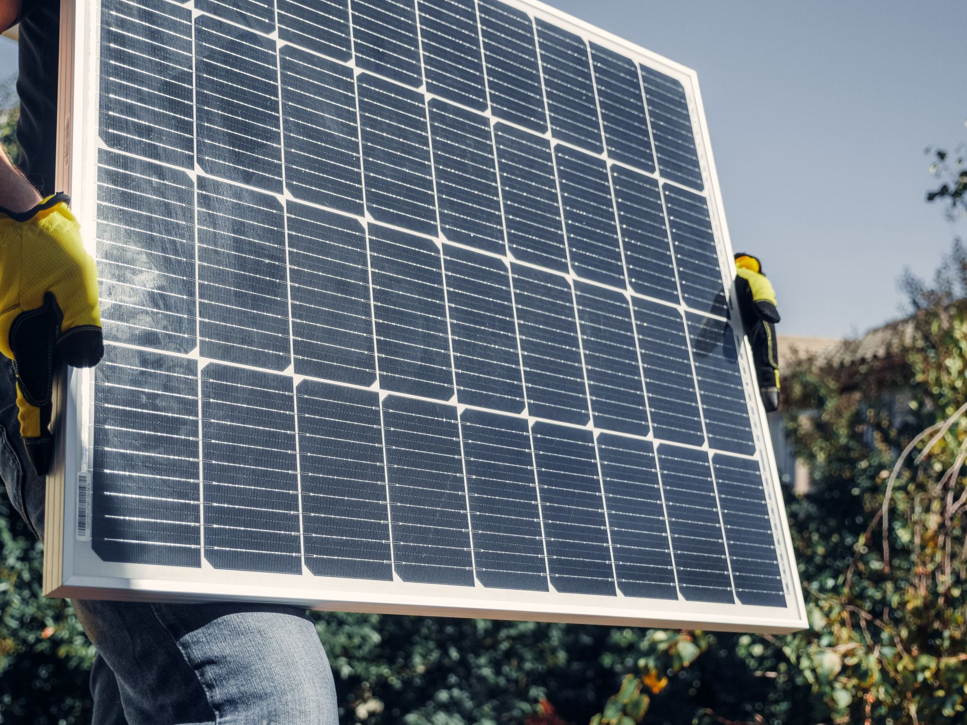 Workers carrying a large solar panel outdoors on a sunny day