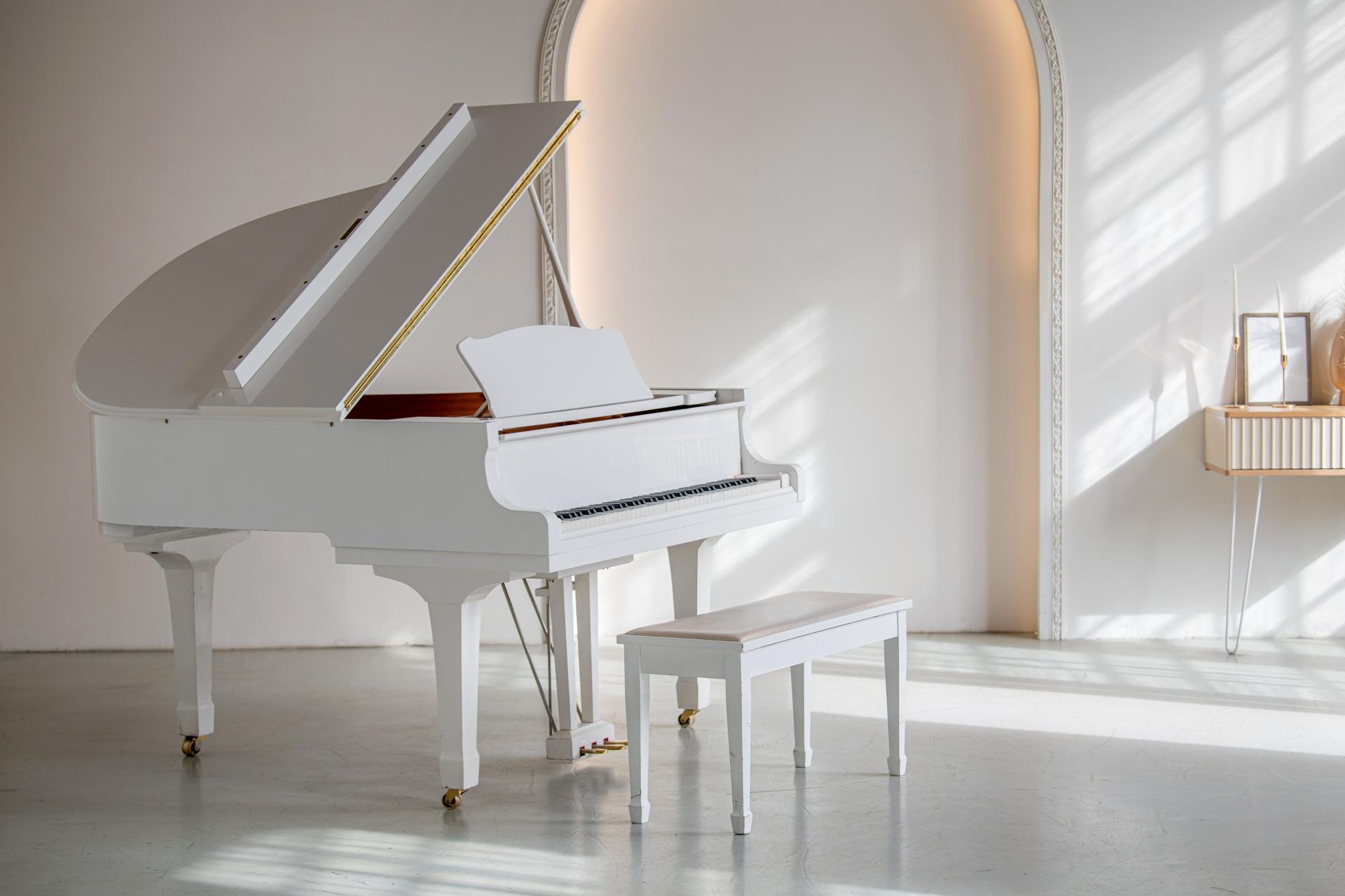 A white grand piano is sitting in a room with a bench.