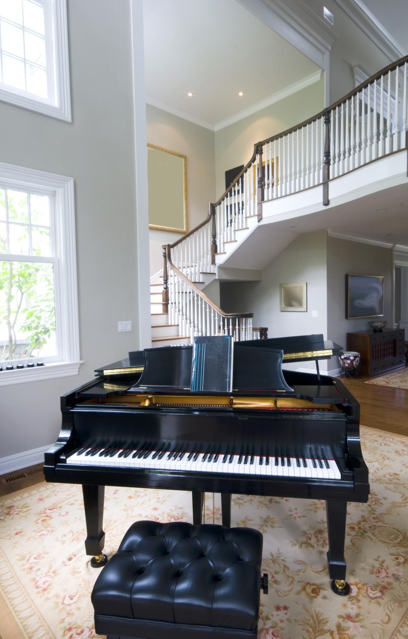 A grand piano is sitting in a living room next to a staircase.
