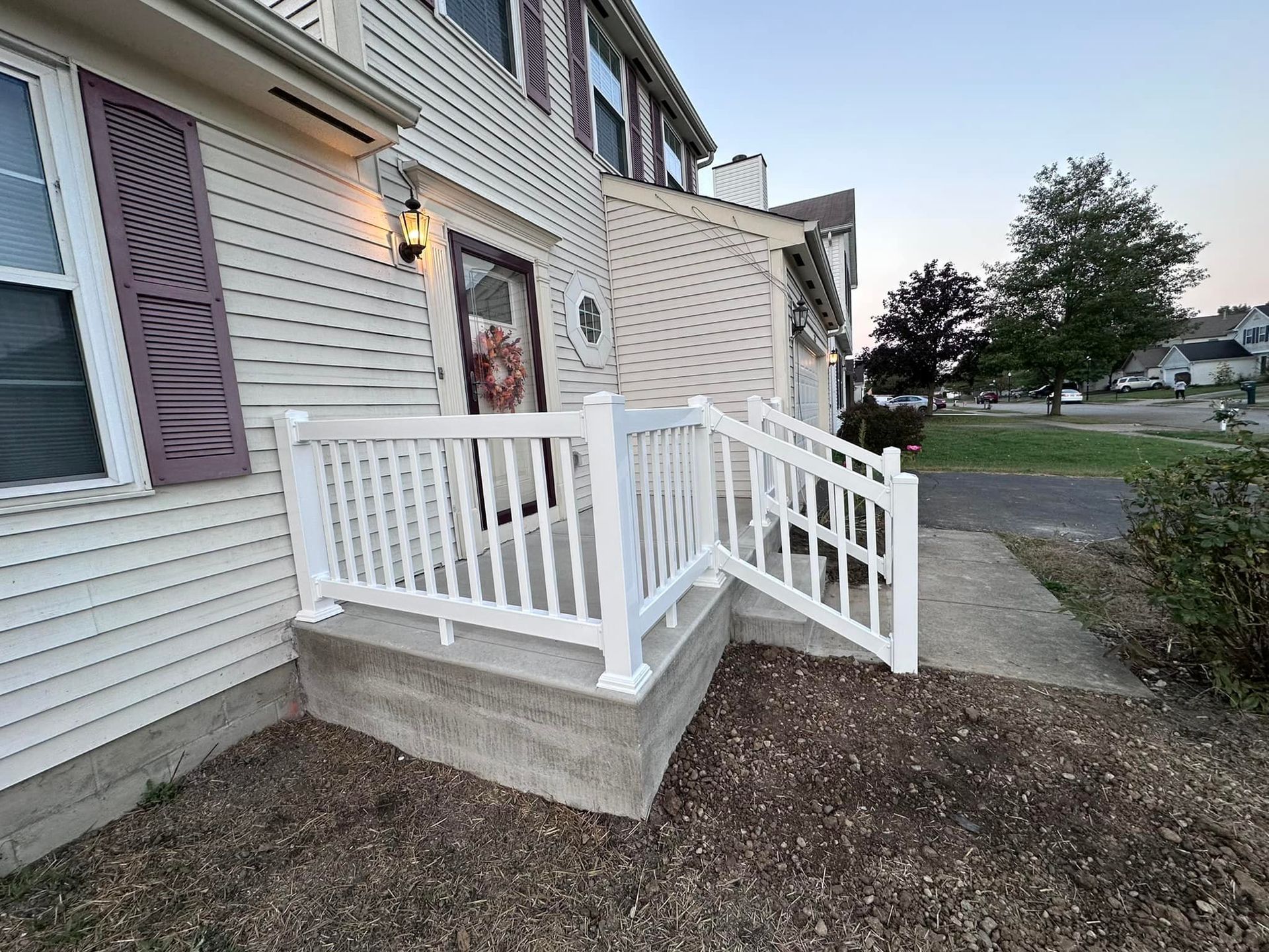 A white porch with a white railing and stairs leading to the front door of a house.