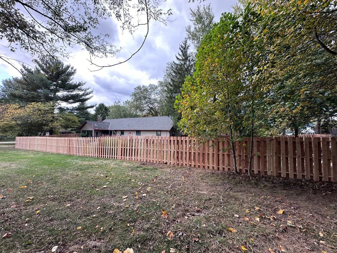 A wooden fence surrounds a grassy yard in front of a house.